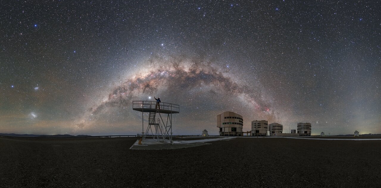 I cieli bui sopra l’osservatorio di Paranal, sede del Very Large Telescope (VLT) dell'ESO, offrono viste mozzafiato così chiare e così piene di stelle che potresti quasi toccarle. In cima a una piattaforma del VLT, l'ambasciatore fotografo dell'ESO Petr Horálek si protende verso un oggetto che spicca nel cielo. Si potrebbe pensare che questo corpo luminoso, come molti altri nel cielo, sia una stella, ma in realtà è un pianeta del nostro sistema solare: il gigante gassoso Giove. Più vicino alla Terra, i quattro telescopi unitari (TU) che compongono il VLT possono essere visti sullo sfondo. Ogni TU ha uno specchio di 8,2 metri. I TU possono operare in sinergia per produrre alcune delle viste più nitide dell’Universo. Ad accompagnare i quattro TU ci sono quattro telescopi ausiliari più piccoli e mobili che hanno specchi da 1,8 metri. Il deserto cileno di Atacama dimostra ancora una volta il suo valore come luogo ideale per il VLT dell'ESO. La lontananza dell'osservatorio significa che l'inquinamento luminoso è minimo o nullo, il che è vitale per l'astronomia e permette di ottenere viste mozzafiato - Crediti: ESO/P. Horálek