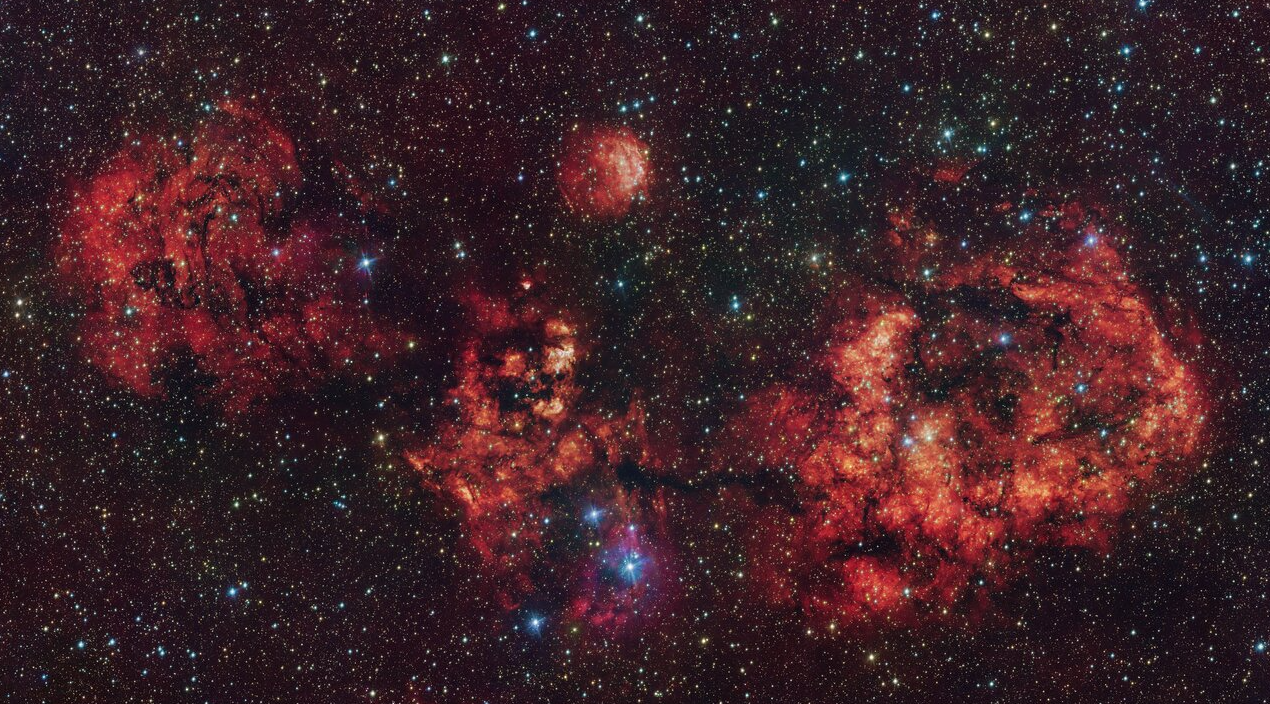 Questa immagine mostra una nube di gas e polvere, a forma di pipistrello cosmico. L'immagine è stata ottenuta principalmente in luce visibile con il VLT Survey Telescope (VST), ospitato presso l'Osservatorio del Paranal dell'ESO in Cile. L'intenso bagliore rosso proviene dagli atomi di idrogeno ionizzati dall'intensa radiazione delle giovani stelle all'interno della nube. L'immagine include anche ulteriori dati infrarossi acquisiti dal Visible and Infrared Survey Telescope for Astronomy (VISTA) dell'ESO, anch'esso al Paranal. Le nubi più evidenti sono RCW 94, che rappresenta l'ala destra del pipistrello, e RCW 95, che ne costituisce il corpo, mentre le altre parti del pipistrello non hanno una designazione ufficiale - Crediti: ESO/team VPHAS+/team VVV