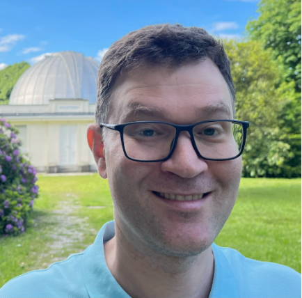 Foto dell'astrofisico Ben Granett. Sullo sfondo il parco e la cupola Zeiss della sede di Merate dell'Osservatorio Astronomico di Brera.